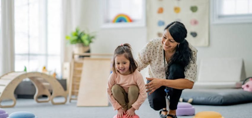 A female Physiotherapist works with a young girl on her balancing during a therapy session.  She is supporting and aiding the young girl as they work together.